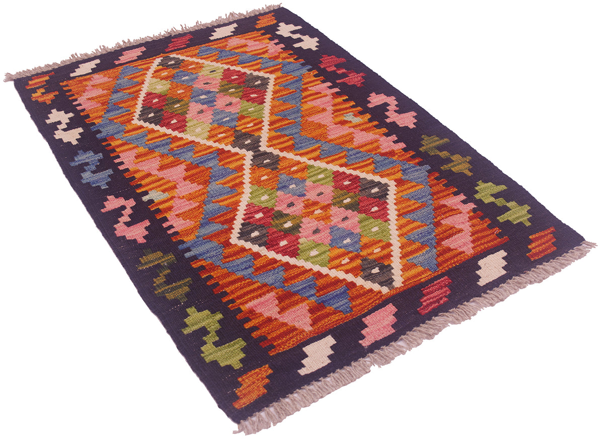 A small Afghan kilim rug with a vibrant geometric pattern, featuring a dark navy blue border and central diamond motifs in orange, pink, green, and blue, finished with fringed edges.
