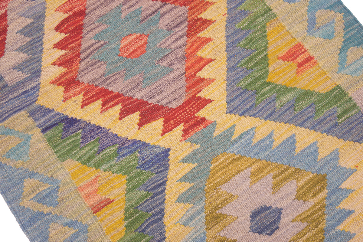 Close-up of a woven geometric kilim rug with a multicolour pattern including red, yellow, green, blue, and beige in a tribal-inspired diamond design.