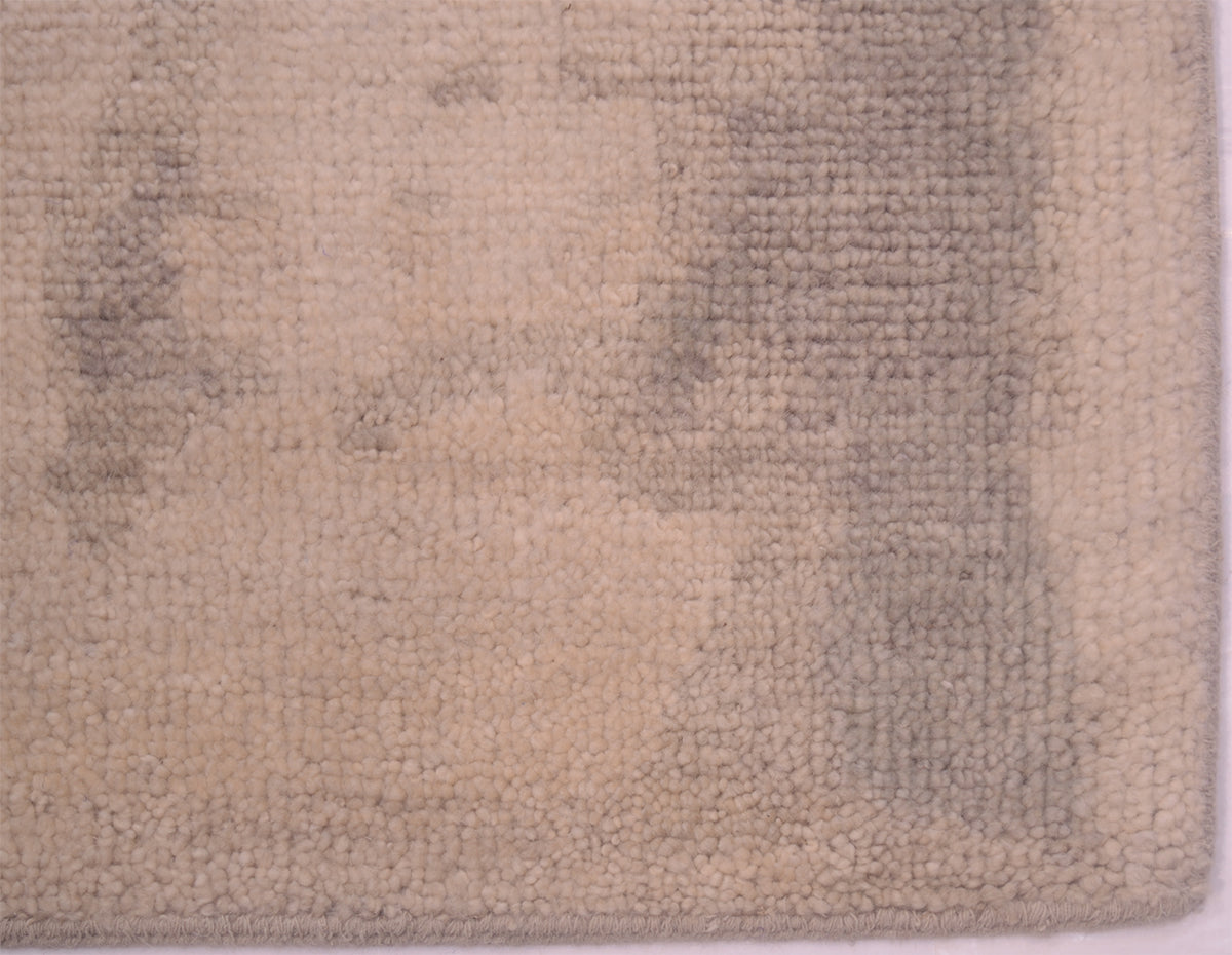 Detail of corner of handknotted carpet in soft greys and cream beiges.No fringes cotton warp threads neatly bound ends and sides