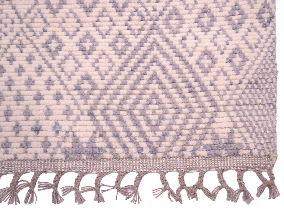 A close-up of a handwoven Afghan Berber design runner with a geometric diamond pattern in light grey-blue and cream, finished with a fringed tassel edge.