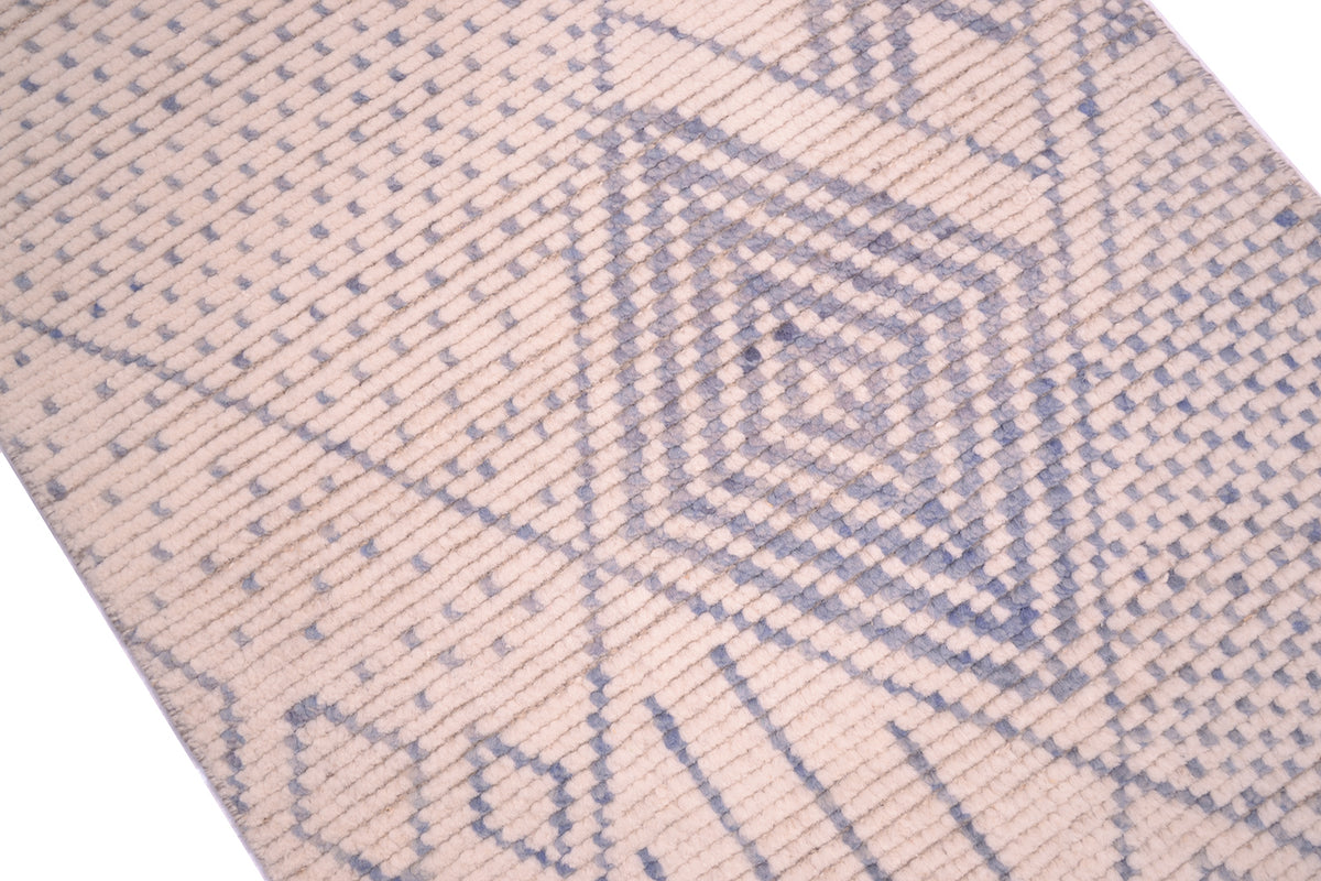 A close-up of a handwoven Afghan Berber design runner rug with a geometric diamond pattern in muted blue-grey on a warm beige / cream background.