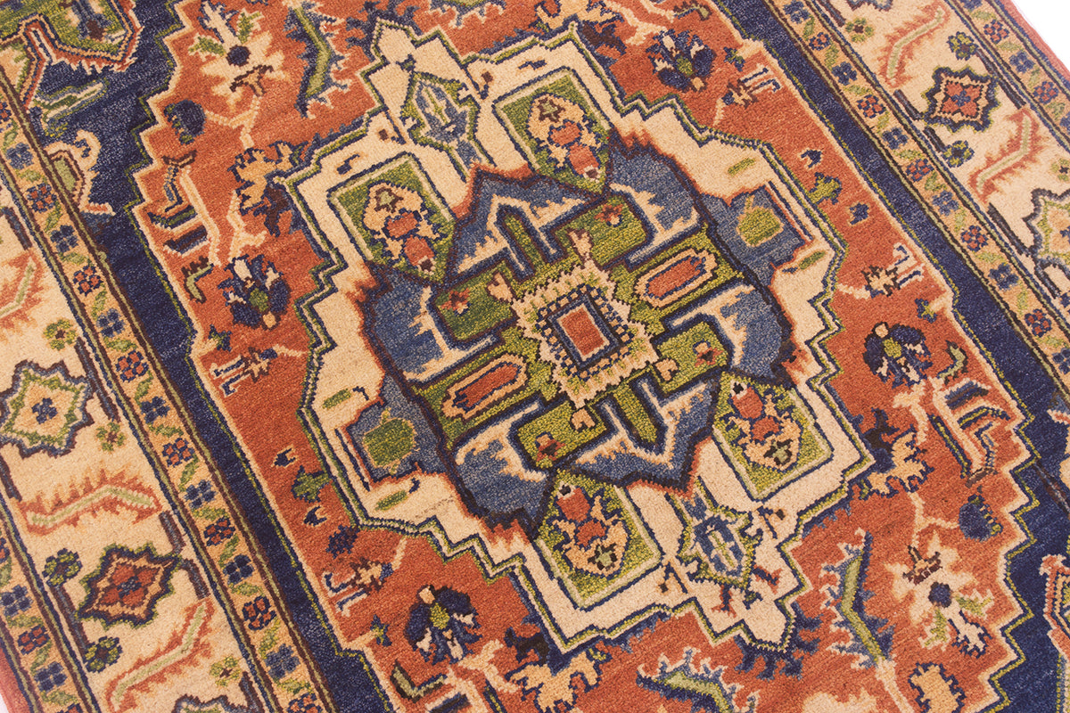 A close-up of a traditional patterned Heriz rug with a central medallion in cream, rust orange, blue, green, and beige.
