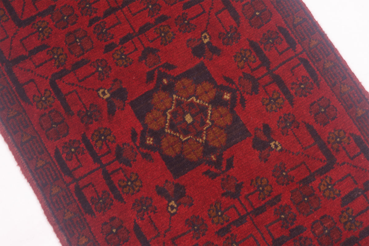 A close-up of a red runner rug with a central medallion and geometric floral motifs in dark brown, black, and muted gold.