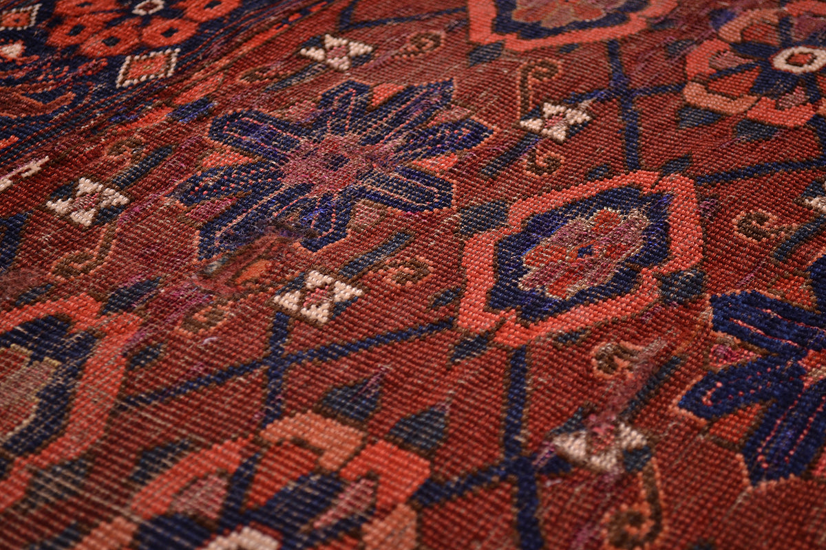 A close-up of an antique handwoven Beshir-Ersari Chuval rug or textile with an intricate geometric and floral pattern in deep red, navy blue, and rust orange.