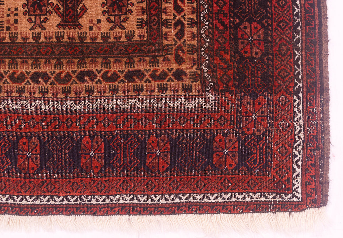 A close-up of a worn antique Belouch prayer rug corner showing red, black, and beige woven borders with geometric and floral motifs and a short fringe along the bottom edge.