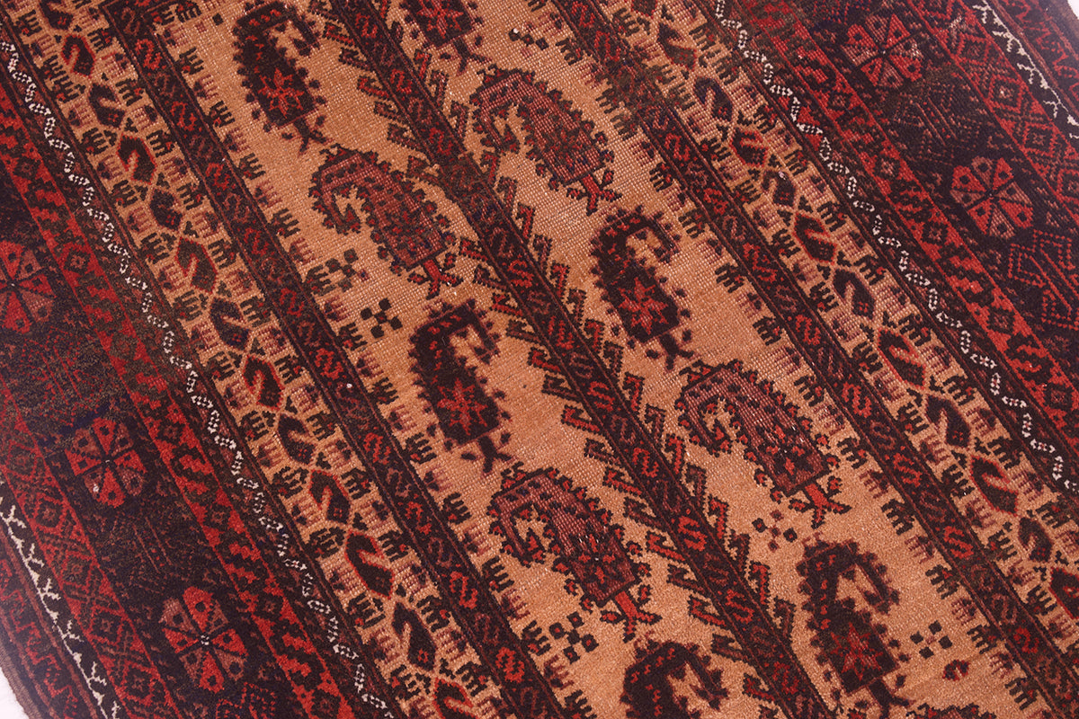 A close-up of a antique Baluchi prayer rug featuring diagonal bands with intricate geometric and paisley (boteh) motifs in dark red, black, and warm terracotta tones.