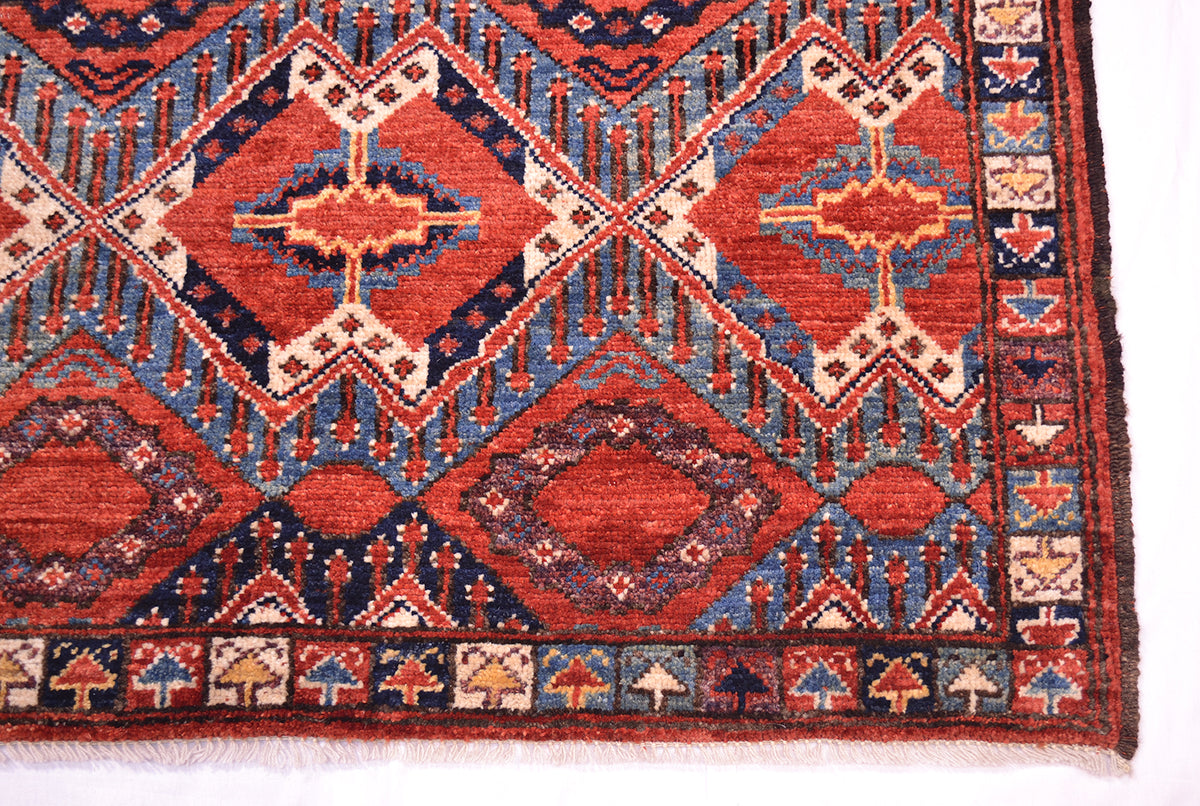 A close-up of a corner of a traditional fine antique style Beshir rug showing rust-red, blue, and beige geometric motifs and borders.