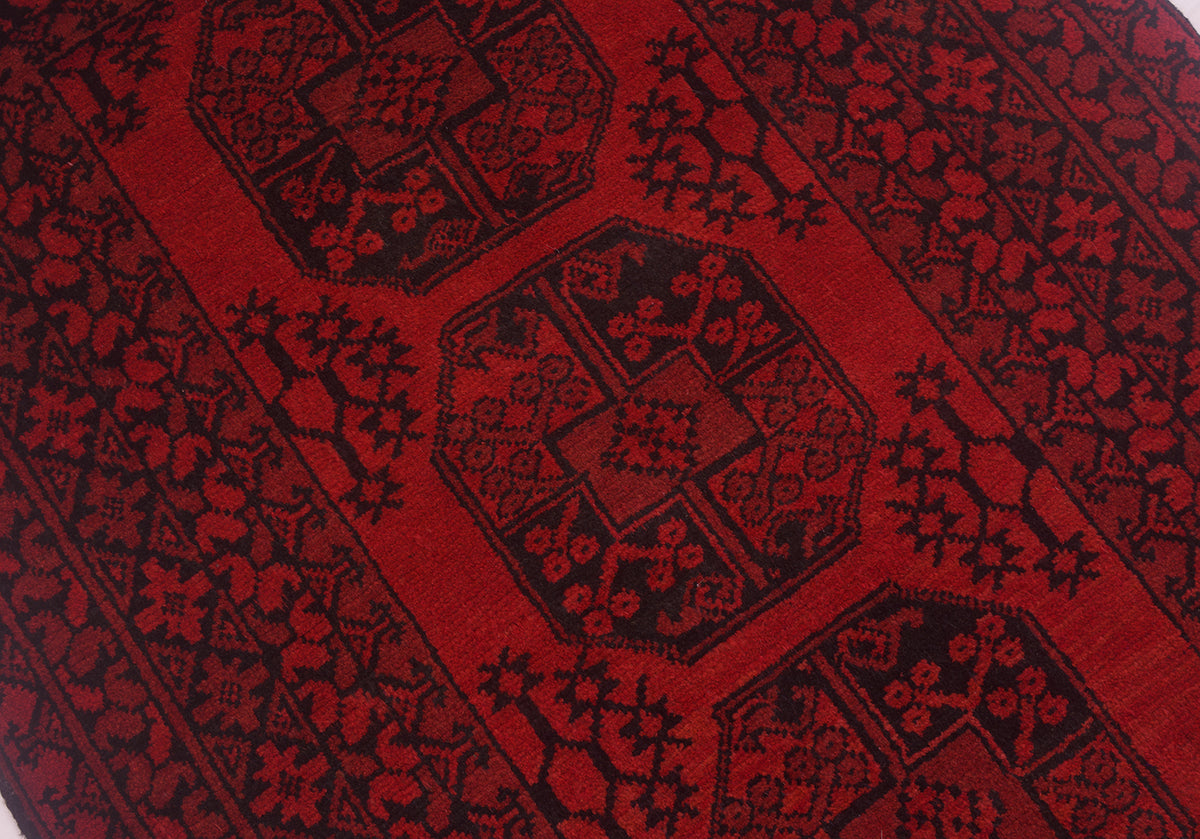 A close-up of a red and black patterned Fil Pai Afghan rug with geometric and floral motifs.