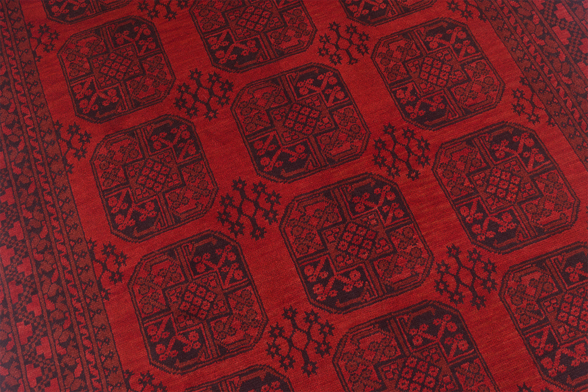 A close-up of a red and black Afghan carpet with a repeating geometric medallion pattern and border design.