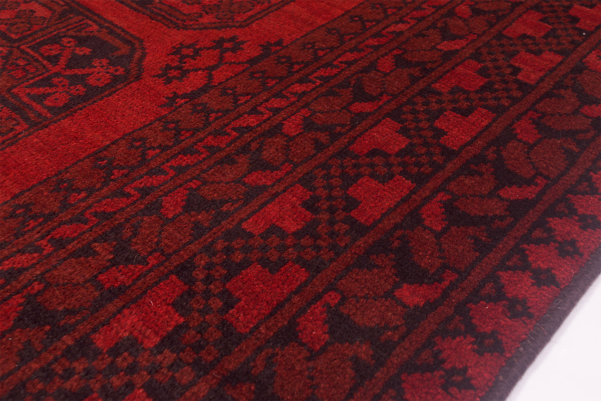 A close-up of a red and black patterned handmade Afghan rug showing detailed woven geometric and floral motifs.