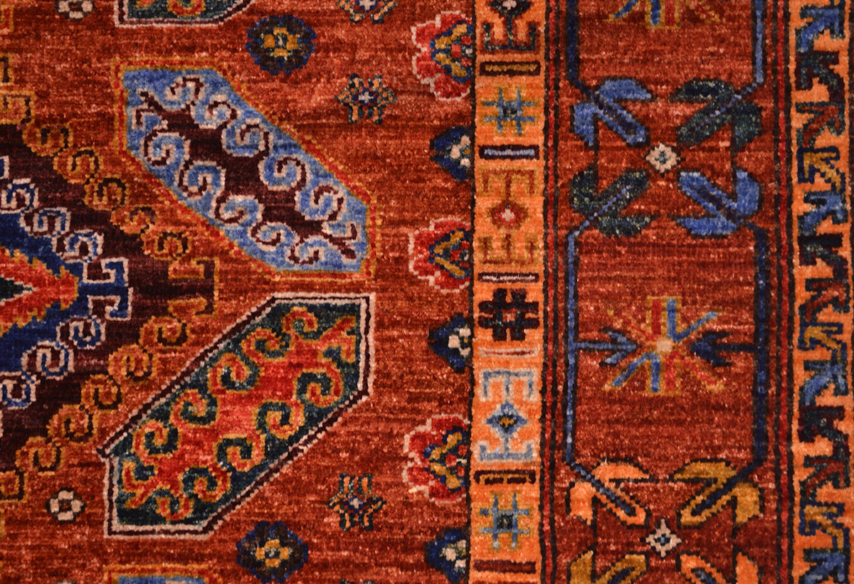 Close-up of a traditional patterned rug with a warm cinnamon field, blue and navy geometric motifs, and a decorative border.