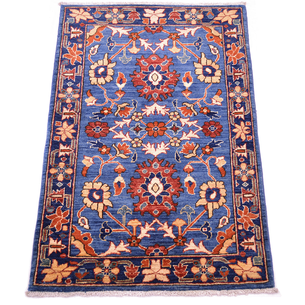 A rectangular traditional blue Aryana rug with a blue field, featuring a central floral medallion and ornate borders in rust red, beige, and cream, shown flat against a white background.