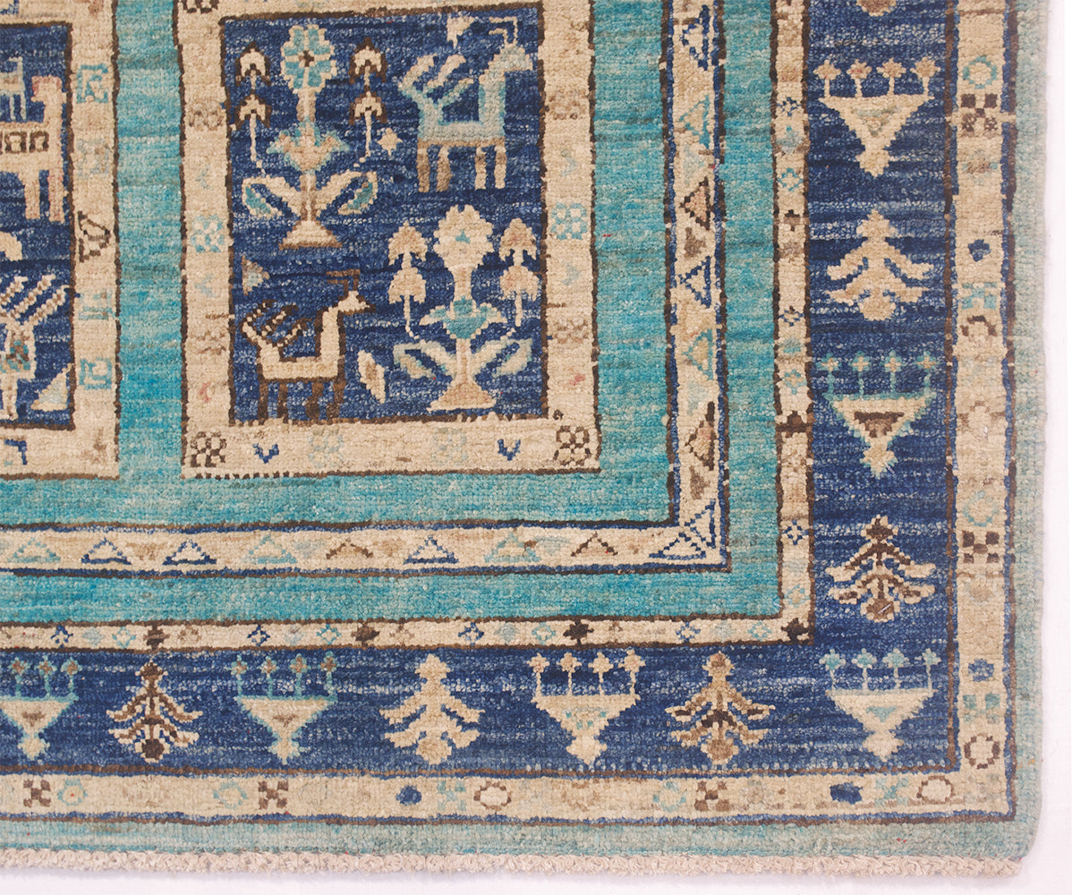 Close-up of a handwoven Afghan rug corner showing geometric and stylised motifs in blue, turquoise, beige, and brown on a white background.