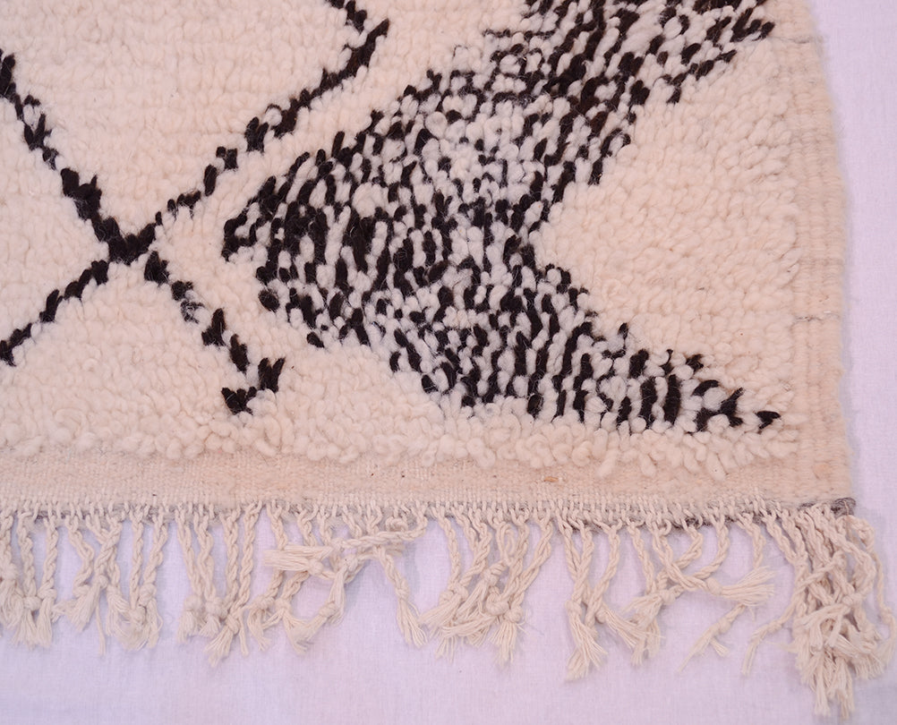 Azilal rug edge with cream fringe and black geometric design on light pink pile.