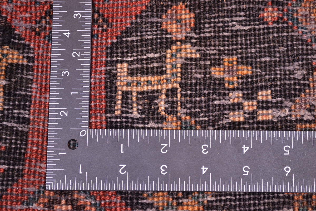 Close-up of the hand-knotted weave of an Old Belouch wide runner rug with a dark charcoal base and orange, rust, and red woven motifs, shown with metal ruler to show scale of the knot density.