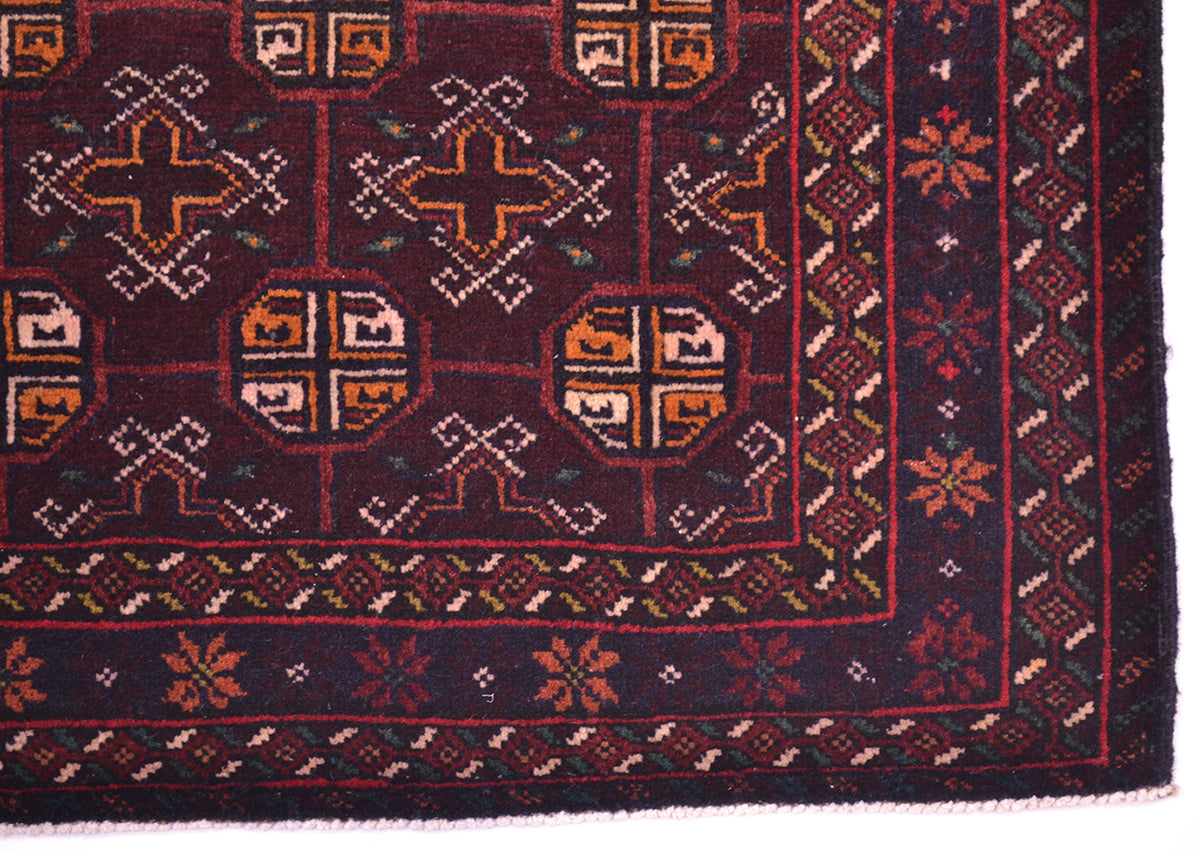 A close-up of a patterned Afghan Belouch mat showing a dark navy blue field with geometric and floral motifs in rust red, orange, beige, and white.