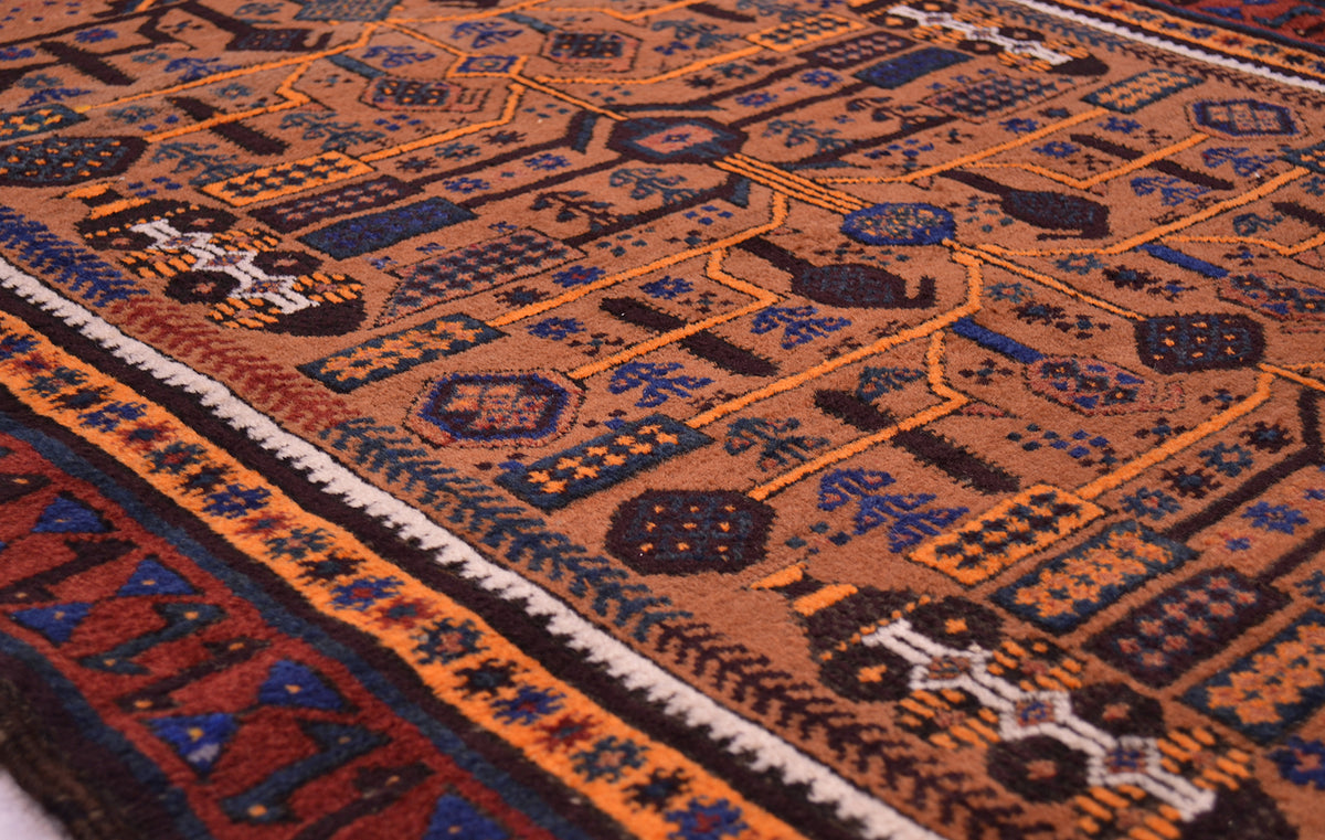 A close-up of a traditional patterned Belouch vintage rug with a warm brown base, featuring geometric motifs in orange, navy blue, black, and cream.