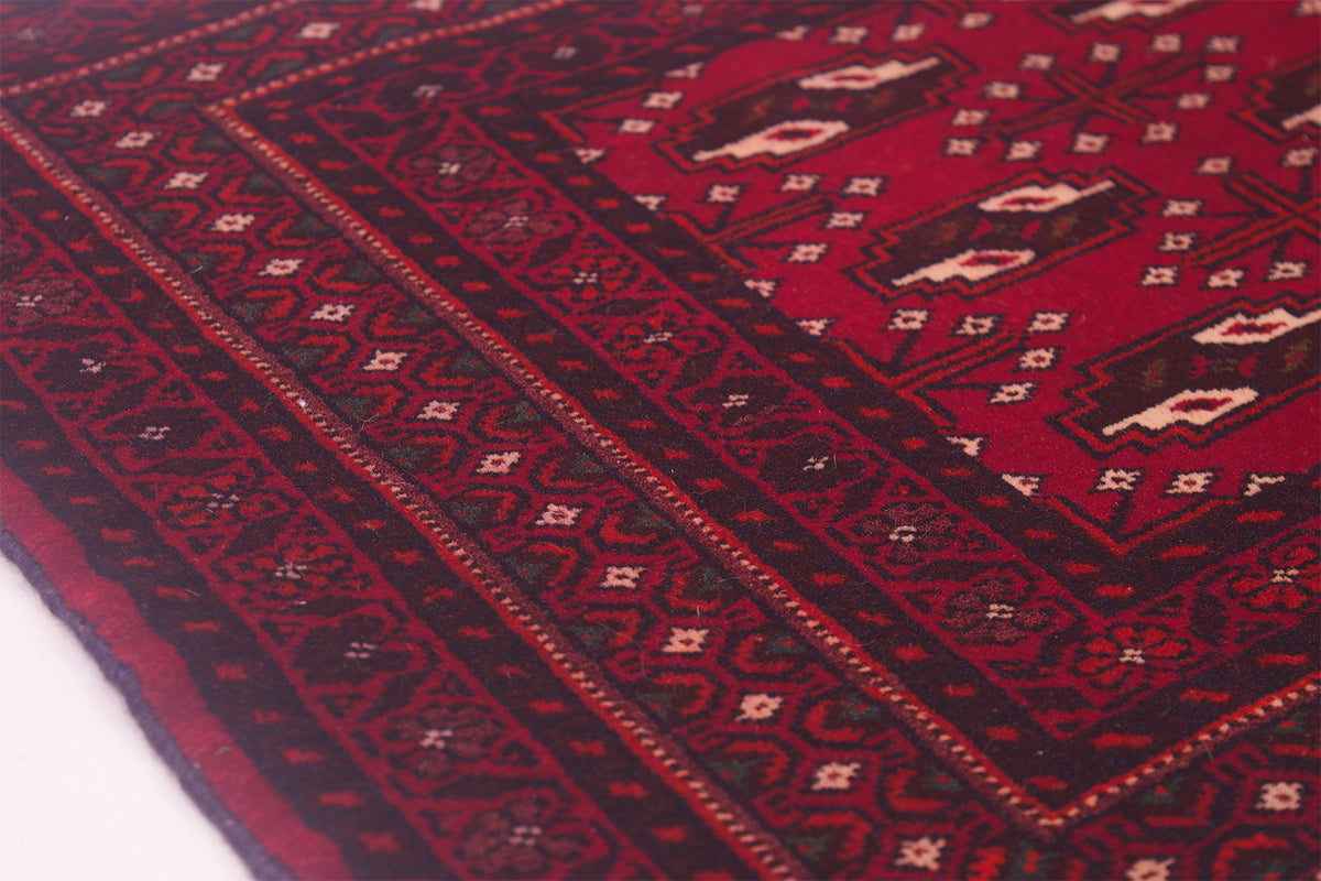 A close-up of a traditional patterned small Belouch rug with a deep red field, dark brown borders, and cream geometric motifs.