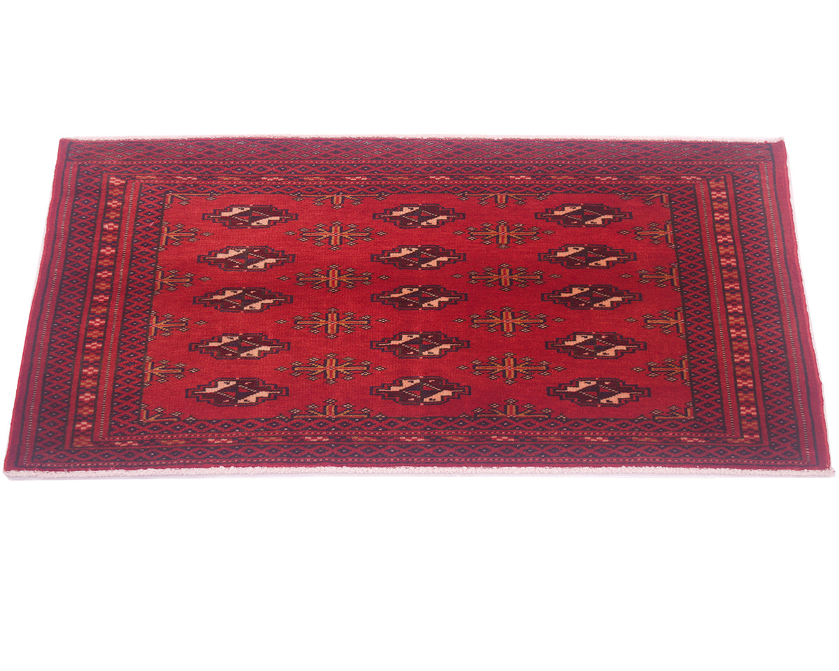 A rectangular red wool mat with a traditional Baluchi design, featuring dark brown and beige geometric motifs and a patterned border, shown flat against a white background.