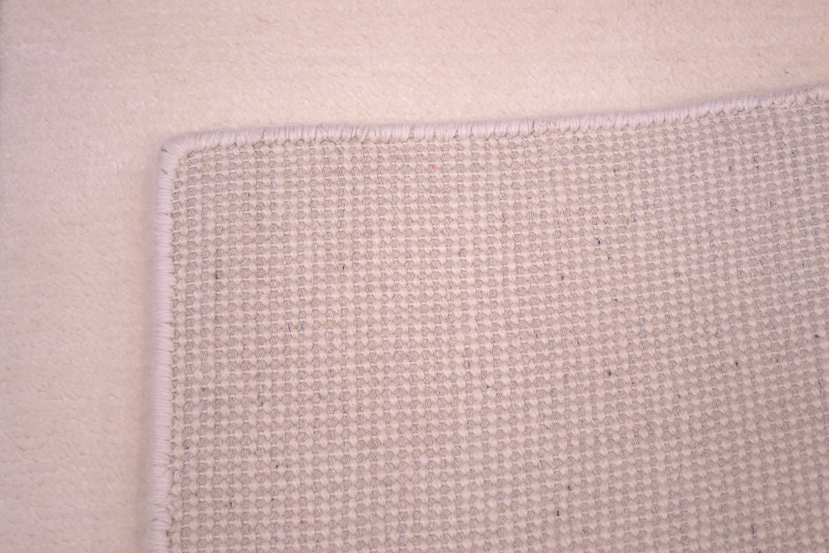 Close-up of the hand-knotted back of a woven rug corner showing a textured plain off-white Indian runner with a matching bound edge.