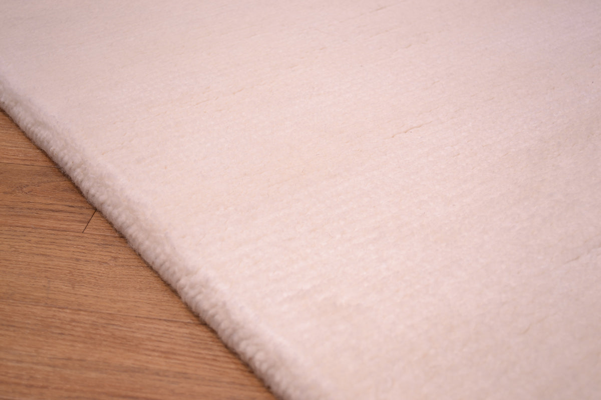 A close-up of a soft, light cream or off-white plush runner rug shown against a light brown wood surface underneath.