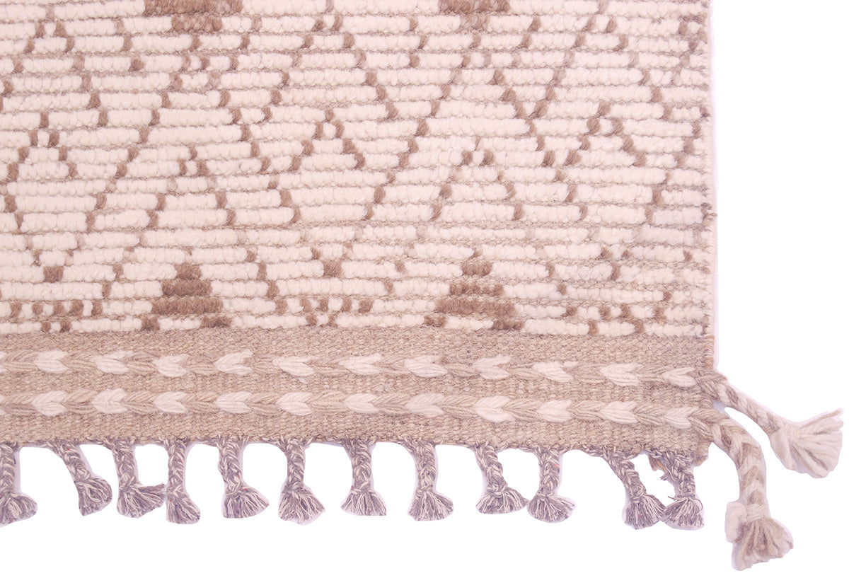 A close-up of a woven rug with a geometric pattern in cream and brown, finished with a braided border and tassel fringe.