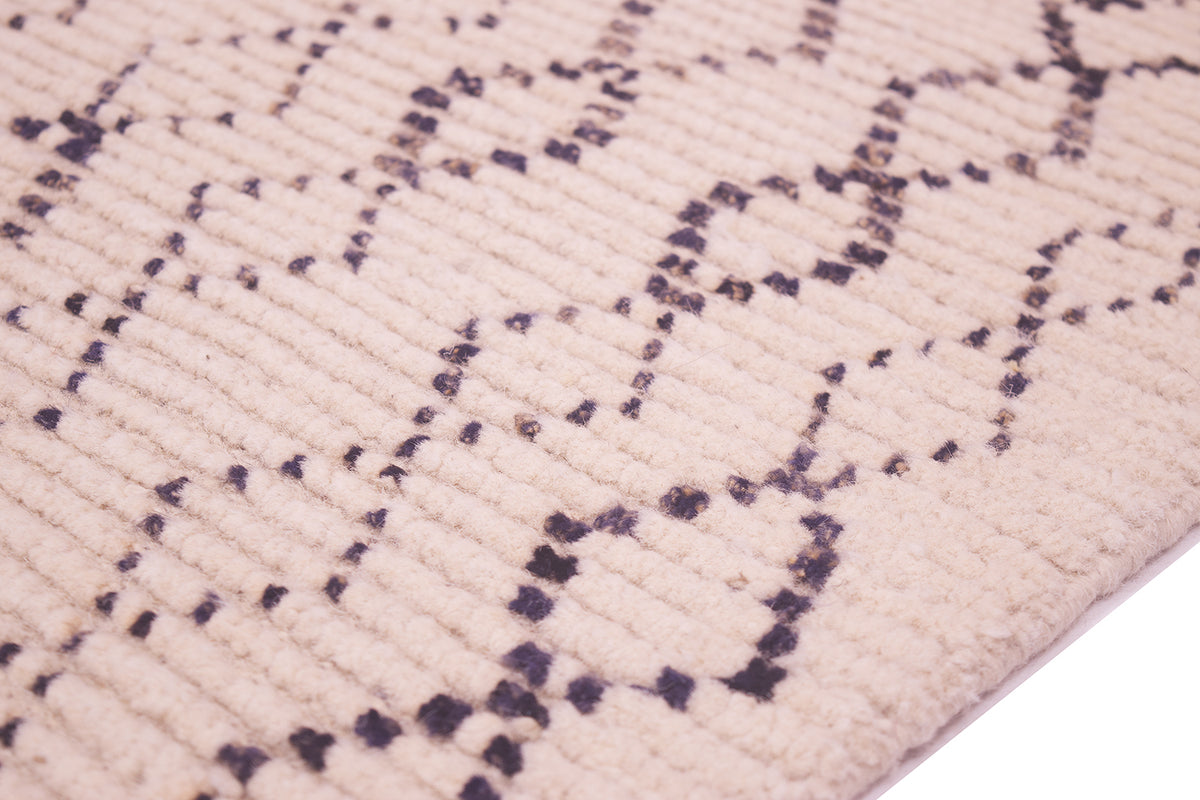 Close-up of a textured rug with a cream-colored ribbed pile and a charcoal geometric diamond pattern.