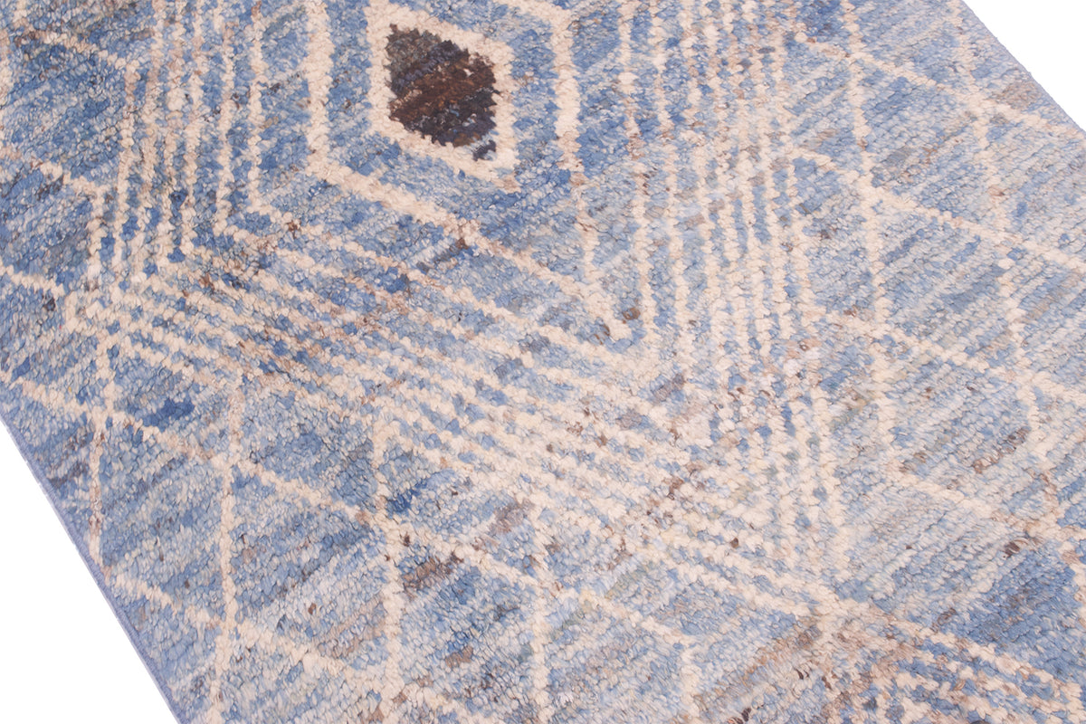 A close-up of a textured area runner/rug with a distressed geometric pattern in light blue, beige, and brown.