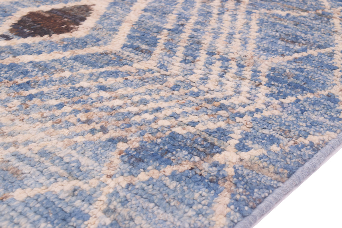 A close-up of a textured area rug/runner with a blue and cream geometric pattern, showing the pile texture and a light blue edge.