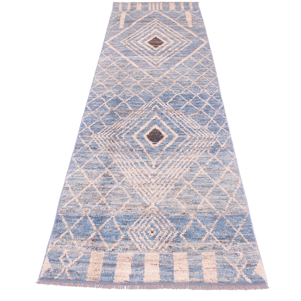 A long rectangular area runner/rug with a blue and beige geometric diamond pattern and fringe on the ends, shown flat against a white background.