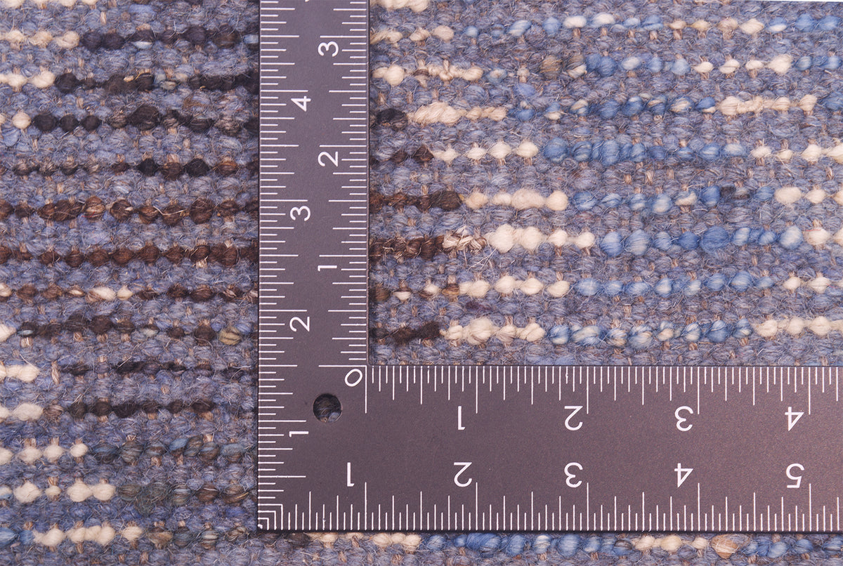Close-up of a the back of woven rug with horizontal striped texture in blue, beige, and brown, shown with a metal ruler for scale.