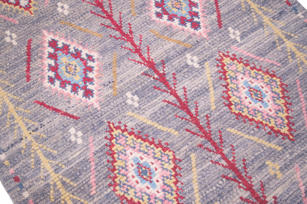 A close-up of a woven handmade Afghan Berber style rug with a grey base and geometric diamond motifs in red, pink, yellow, blue, and white.