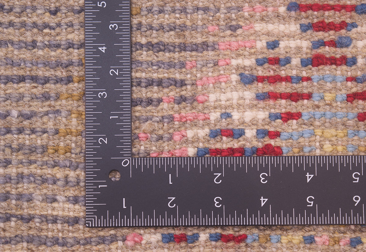 Close-up of the hand-knotted weave of a textured Afghan Berber design rug with a dark ruler placed along the edge to show scale of the weave, featuring a multicolour pattern of beige, blue, pink, and red.