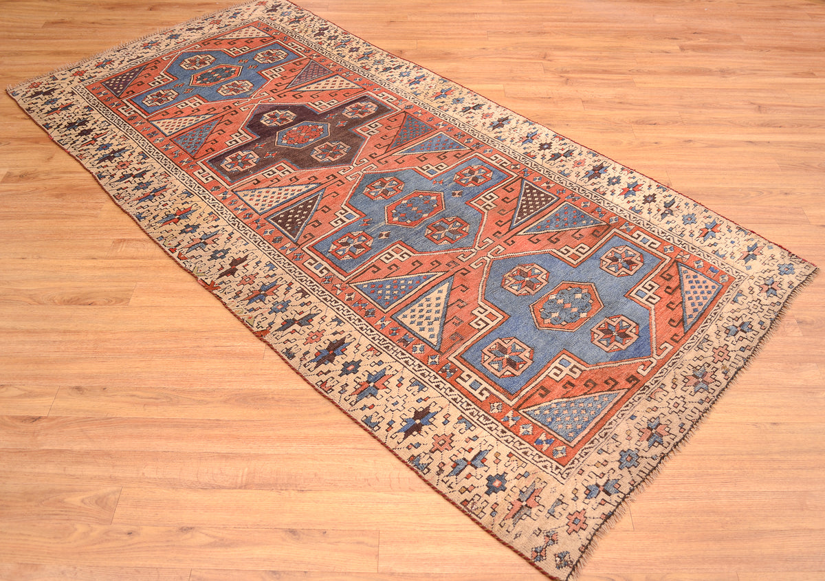Antique Bergama rug laid diagonal on wood floor, featuring rust, blue, and beige motifs