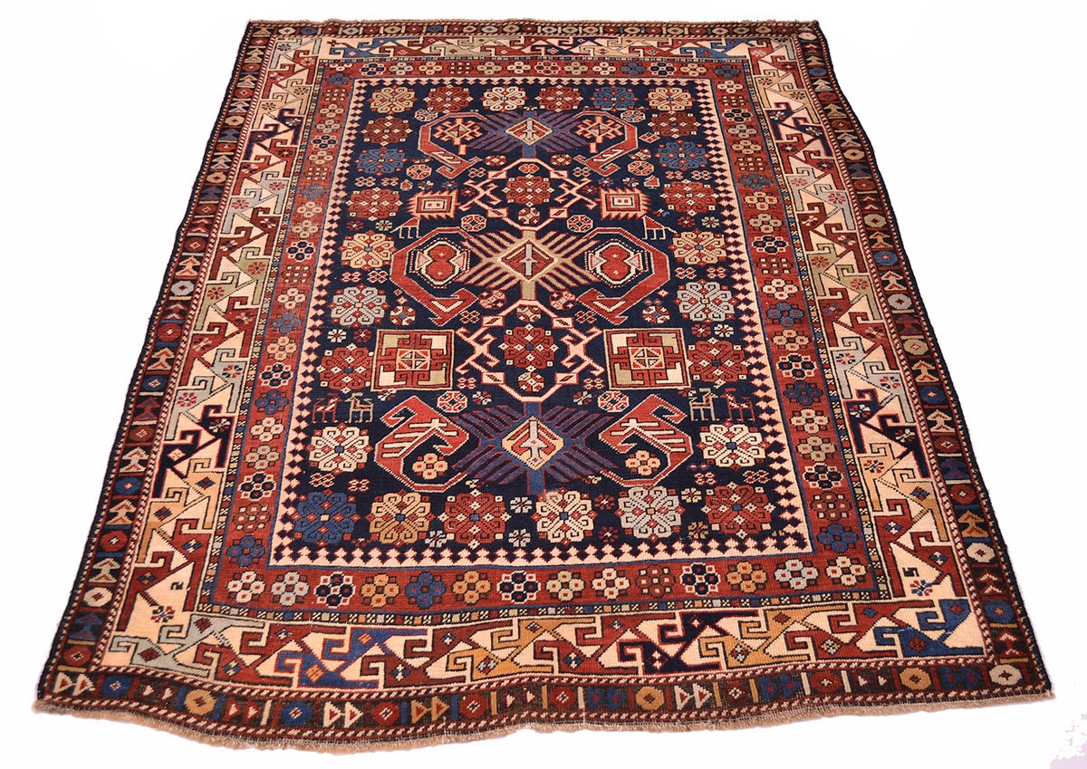 Antique rug with navy and red central panel, cream corner ornaments, detailed patterned frame.