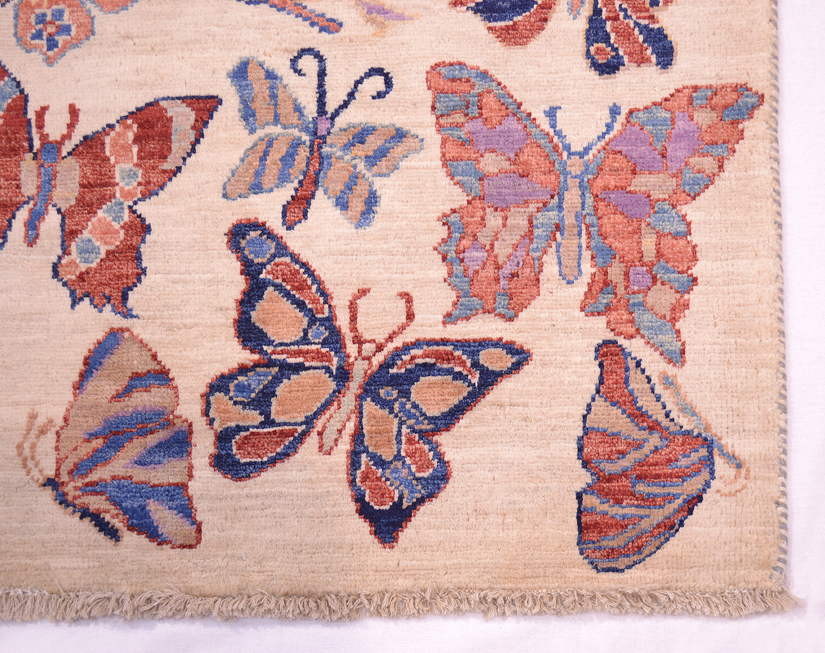 Close-up of a corner of an Afghan Aryana butterflies rug woven rug with a cream background and multiple butterfly motifs in blue, rust orange, and purple, showing the fringe edge.