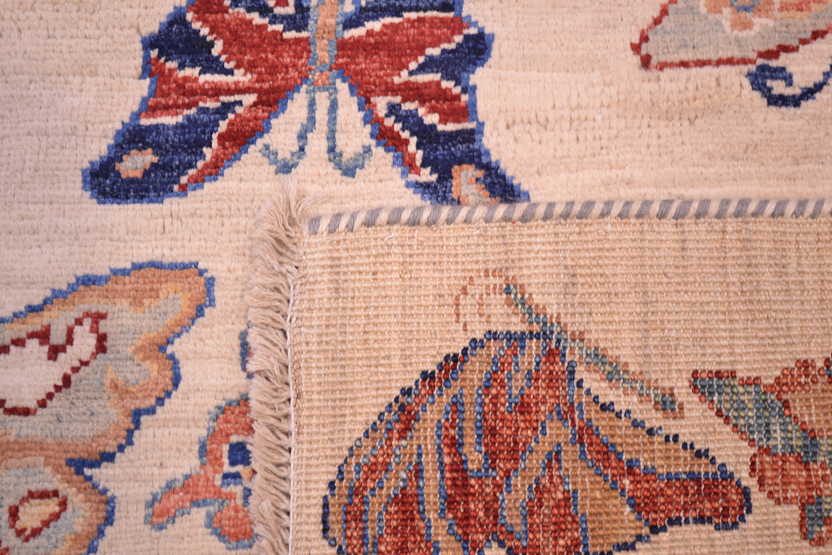Close-up of a hand-knotted Afghan butterfly rug corner showing a cream base with multicoloured butterfly and floral motifs in red, blue, and orange, plus a fringed edge.
