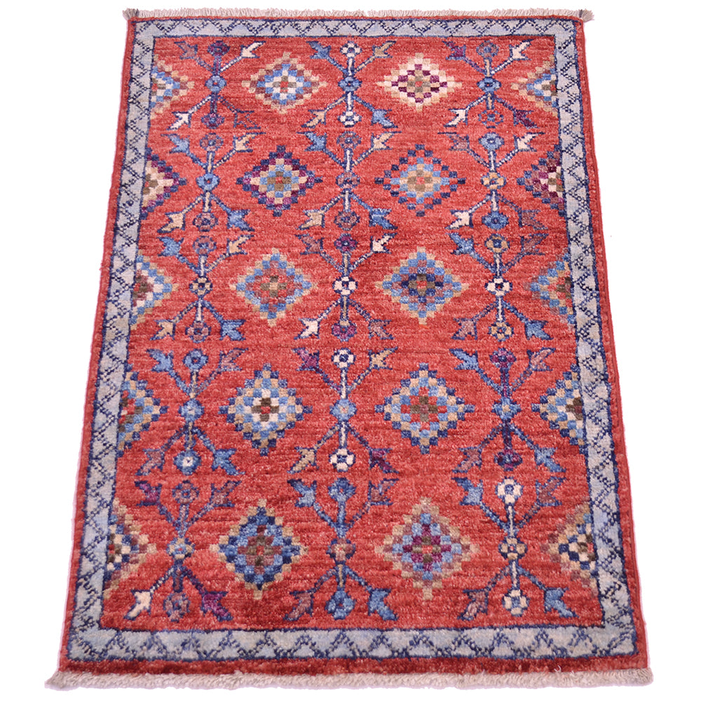 A rectangular hand-woven small Afghan Chobi rug with a traditional geometric pattern, featuring a dominant terracotta red field, blue and beige diamond motifs, and a patterned border on a white background.