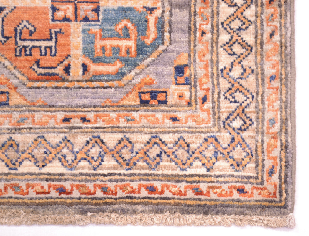 Close-up corner view of a patterned Afghan handmade mat showing cream, orange, blue, and grey woven sections with a fringed edge.