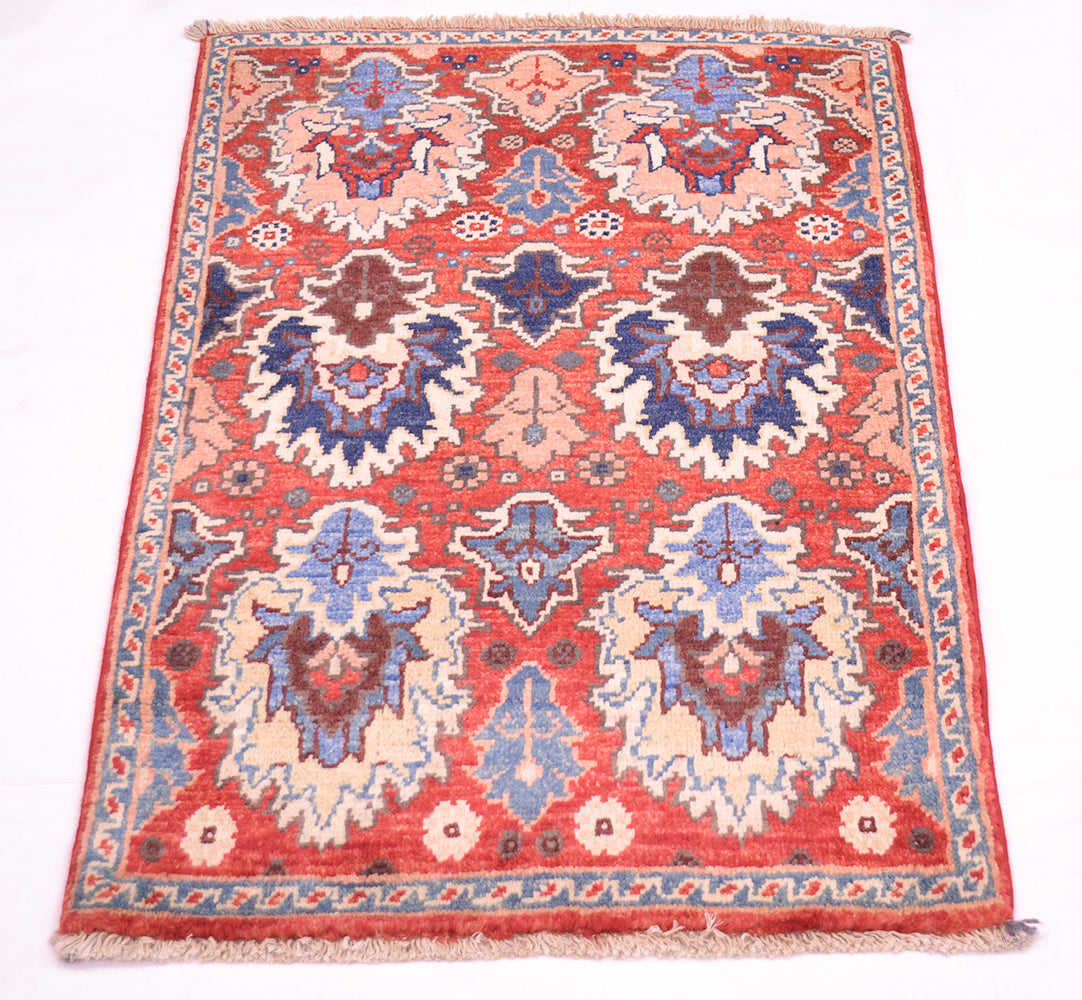 A rectangular traditional Afghan Chobi mat / small rug with a red field, featuring large central medallions in blue, beige, and brown, finished with a patterned border and fringed edges.