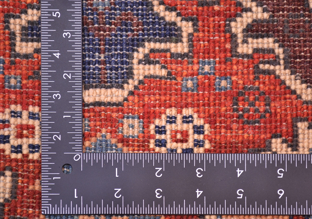 Close-up of the back of a hand-knotted patterned Afghan Chobi mat / small rug with a dark ruler placed along the left and bottom edges to show scale of the knot density, featuring a red, navy, beige, and brown ornamental design.