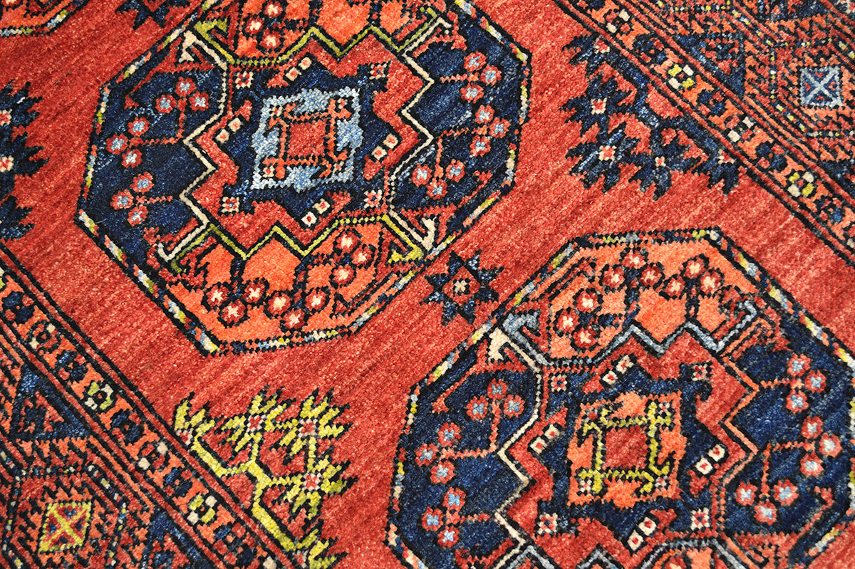 A close-up of a traditional patterned long Afghan Ersari runner rug featuring a warm red-orange field with large hexagonal medallions in navy blue, orange, yellow, and light blue.