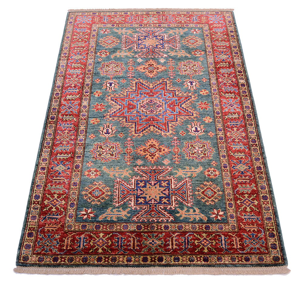 A rectangular traditional area Kazak rug with an intricate geometric and floral pattern, featuring a green centre field, red borders, and blue and beige accents, shown flat against a white background.
