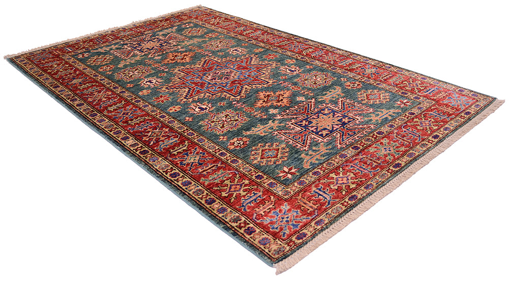 A rectangular area rug with a traditional Persian-style pattern, featuring a dark teal-blue center field, red borders, and cream fringe, shown from an elevated angle on a white background.