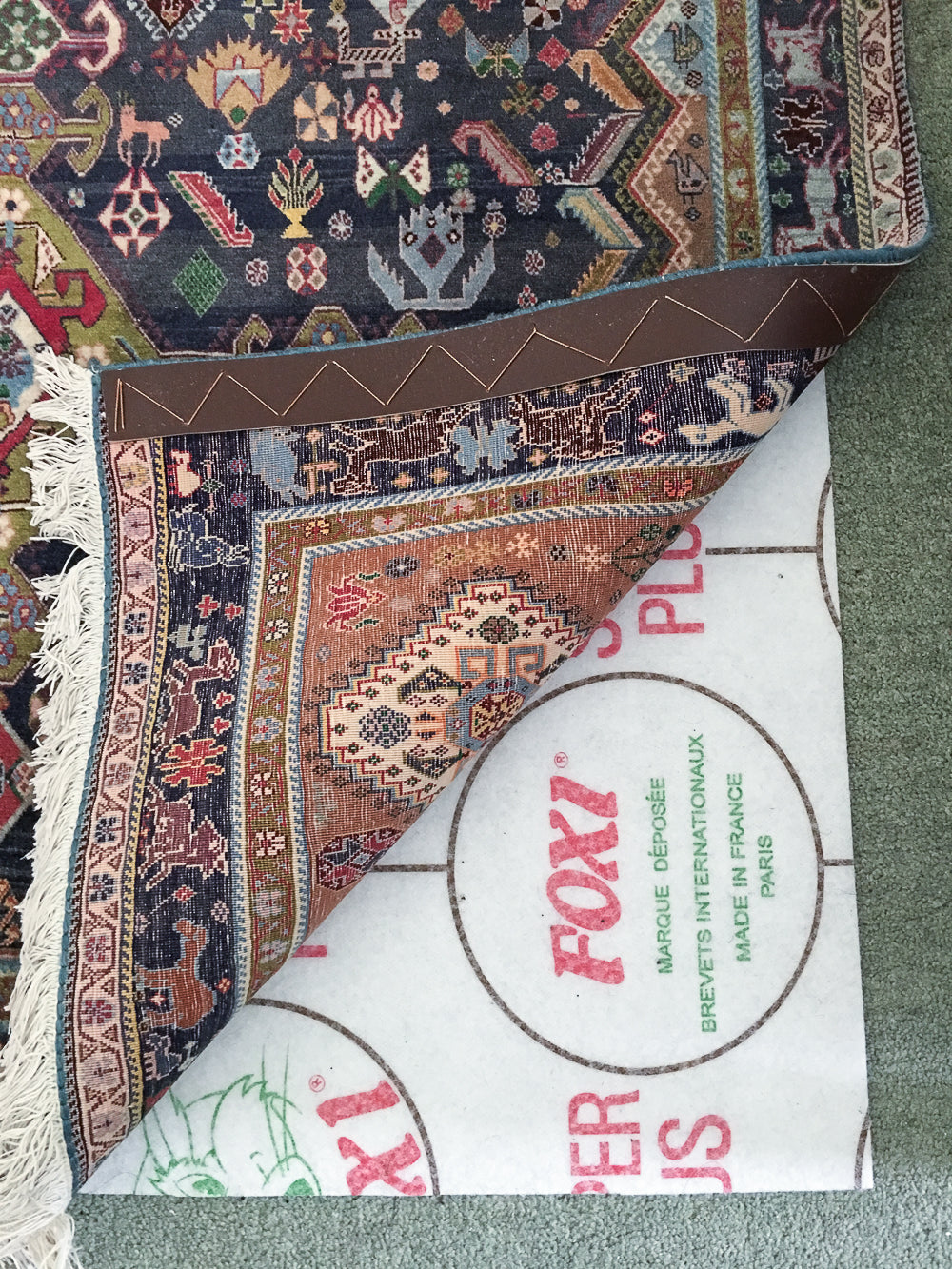 Foxi Rug Underlay in position to stop Qashquli Rug from moving on a green carpet.