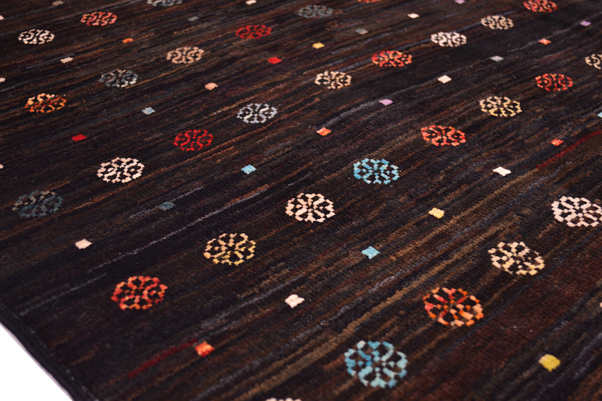 A close-up of a dark brown Handmade Afghan Gabbeh Rug with a subtle texture, decorated with repeating circular medallion motifs in red, blue, orange, and cream, interspersed with small coloured squares.