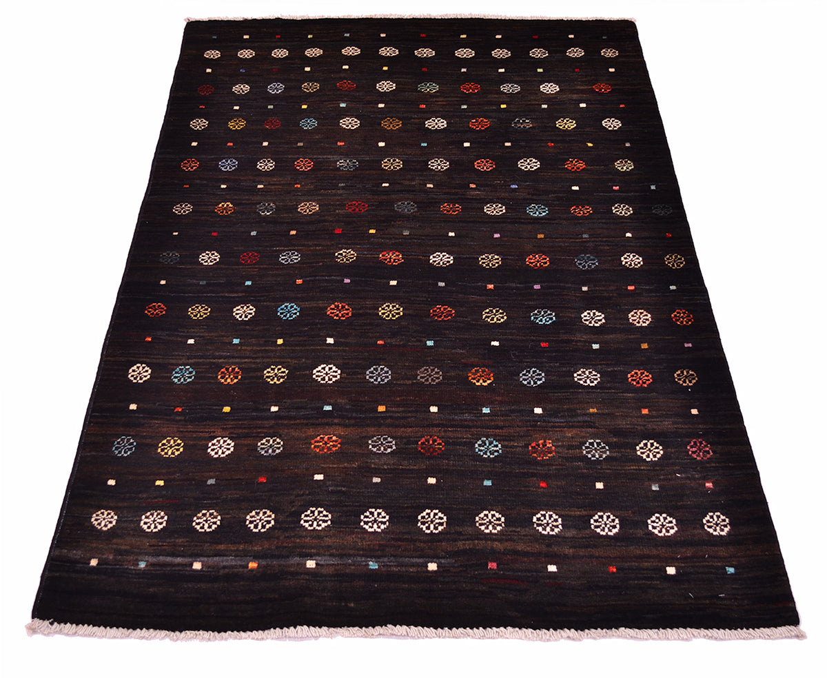 A rectangular dark brown-nearly black wool Afghan Gabbeh area rug with a woven geometric pattern of small circles, dots, and floral-like motifs in beige, red, blue, and white, finished with a light pink fringe.