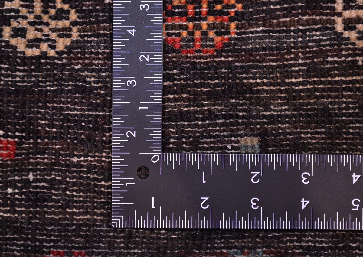 Close-up of a dark patterned Handmade Afghan Gabbeh rug with a metal L-square ruler placed over it to show scale of the knot density, highlighting the woven texture and colour details.