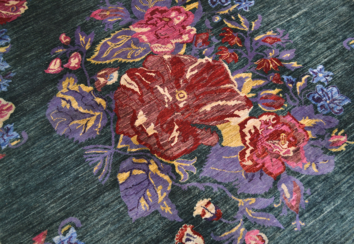 A close-up of a woven Afghan Gul Ferang floral rug with a dark teal-green background and large red, pink, purple, and blue flowers with yellow accents.