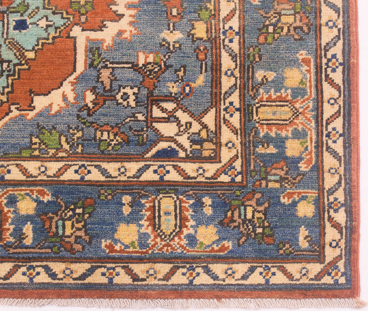Close-up of an ornate Afghan Heriz area rug corner showing a blue field with cream, rust, and green geometric and floral motifs, plus a patterned border and fringe.